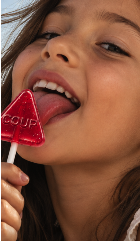 A girl by the sea tasting a red COUP lollipop embossed with COUP